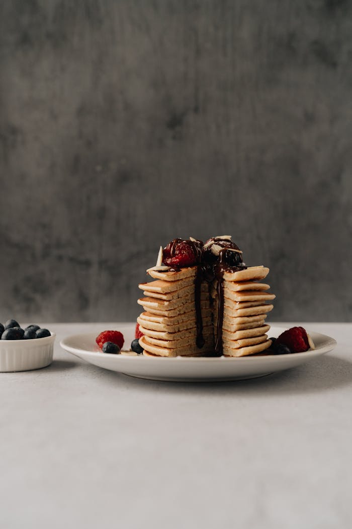 A vertical stack of pancakes topped with berries and chocolate, perfect for food presentations.